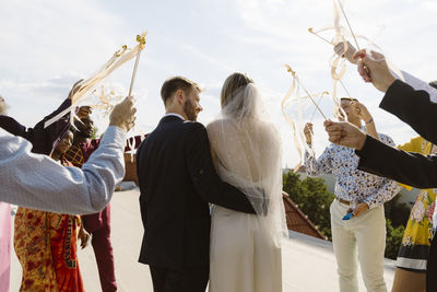 Rear view of groom walking with arm around bride amidst guests at wedding ceremony