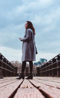 Surface level view of woman standing on footbridge against cloudy sky