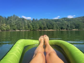 Personal perspective of female tanned legs resting on an inflatable mattress floating on the lake 