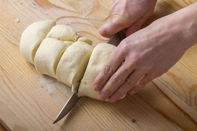 Cropped hands slicing pasta dough on table