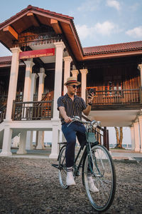 Portrait of young man on bicycle against building