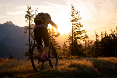 Man riding bicycle on field against sky during sunset