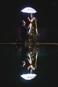 Woman standing by swimming pool at night