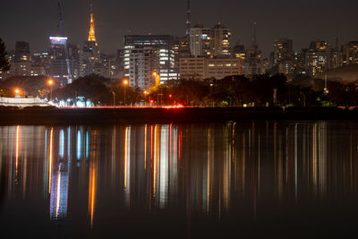 Illuminated buildings by river against sky at night