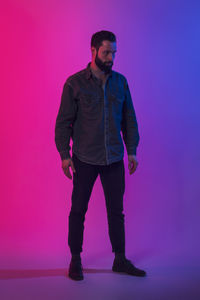 Full length of young man standing against pink background