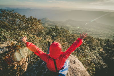Woman with arms outstretched sitting on cliff against mountains