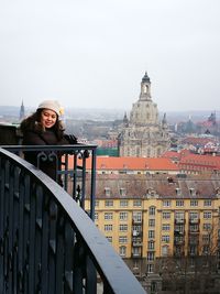 Portrait of woman standing by railing against buildings in city