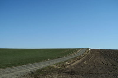 Scenic view of road amidst field against clear blue sky