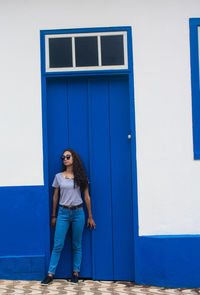 Portrait of young woman standing against blue door