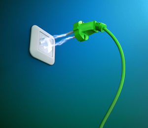 Low angle view of electricity supplying from outlet to plug against blue background