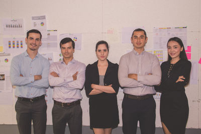 Portrait of smiling colleagues standing against wall in office