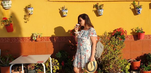 Beautiful woman having coffee while standing against yellow wall