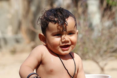  a small cute indian hindu baby looks at the camera while taking a bath with unclothed