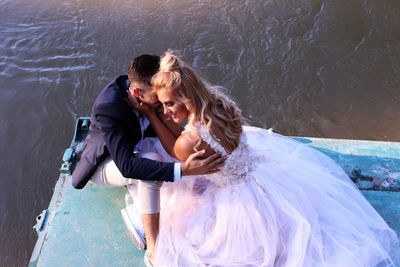 High angle view of smiling bride and groom romancing on pier over lake