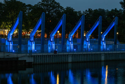Illuminated built structure by river against sky at night