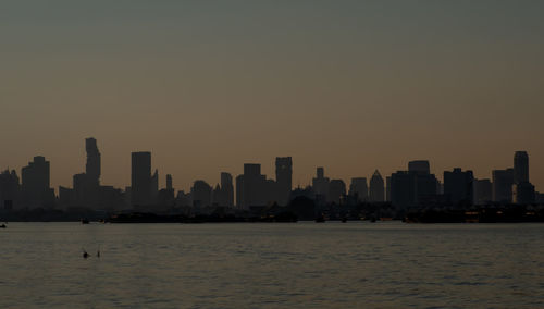 Sea by buildings against clear sky during sunset