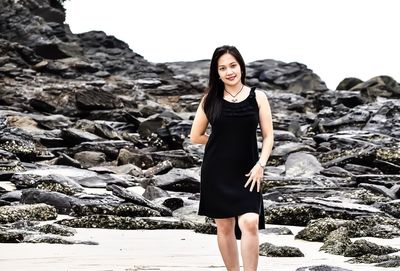 Portrait of young woman standing against rocks at beach