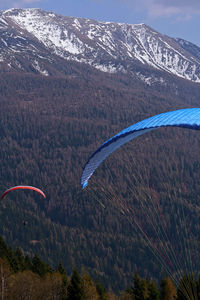 Scenic view two paragliders flying sorrounded by snowcapped mountains against sky.