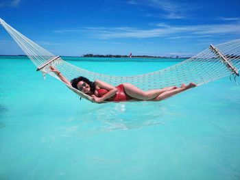 Portrait of woman relaxing on hammock over blue sea 