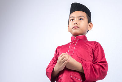 Cute boy wearing maroon traditional clothing standing against white background