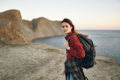 Portrait of young woman standing at sea shore against sky