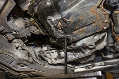 Draining used diesel engine oil from an oil pan into a metal container in a car workshop.