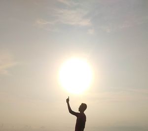 Silhouette man with arms raised against sky during sunset