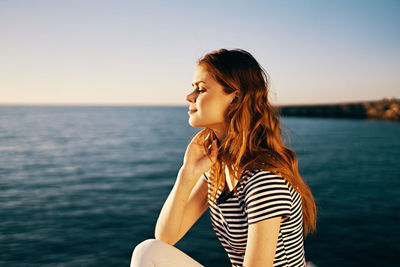 Side view of young woman against sea against sky