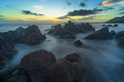 Rocks in sea against sky during sunset