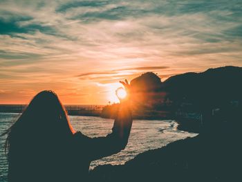 Rear view of woman showing ok sign at beach against sky during sunset