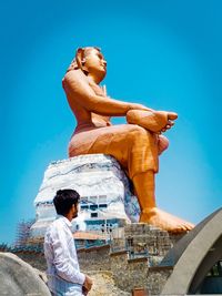 Low angle view of boy on cross against blue sky