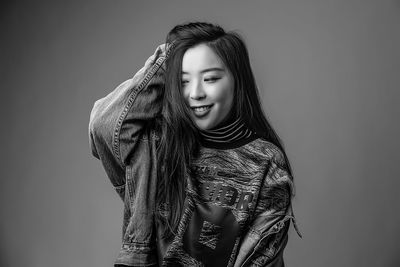 Smiling young woman with hand in hair standing against gray background