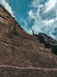 Low angle view of man standing on rock against sky