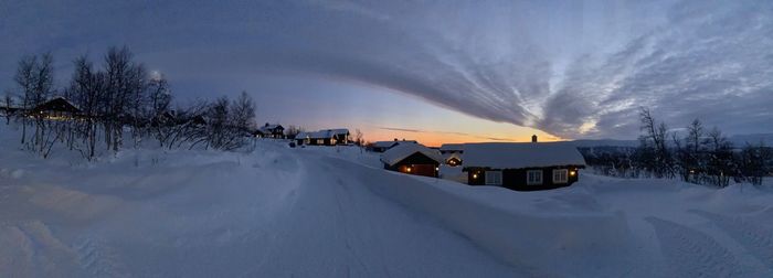 Snow covered houses and trees against sky during sunset