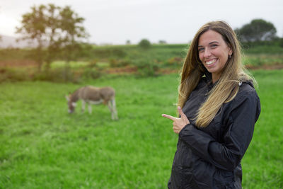 Portrait of smiling young woman gesturing while standing on field