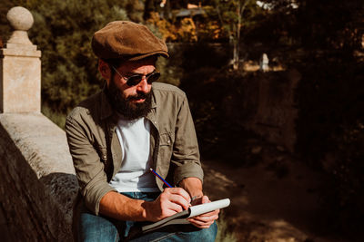 Man writing in book while sitting outdoors