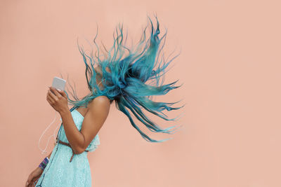 Cropped hand of woman holding flower against pink background