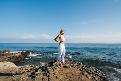 Female athlete standing on rocky beach, looking towards the sun