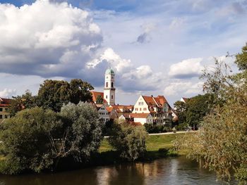 Plants by river and buildings against sky