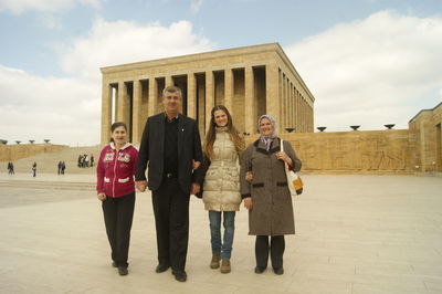 Portrait of friends standing against built structure against sky