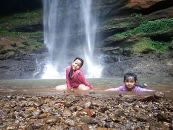 Portrait of little girl sitting on rock against waterfall