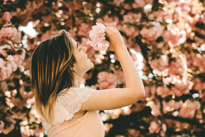 Side view of woman holding flower against tree