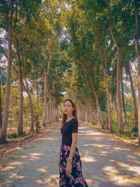 Young woman standing on road amidst trees in forest