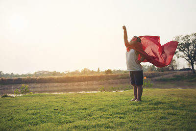 Cheerful boy wearing cape while standing at park against clear sky