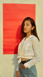 Young woman standing against red wall