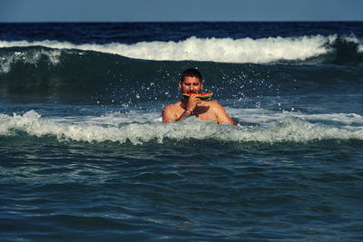 Portrait of man eating watermelon standing at sea