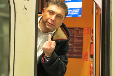 Portrait of man showing obscene gesture while standing in train