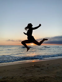 Man jumping at beach against sky during sunset