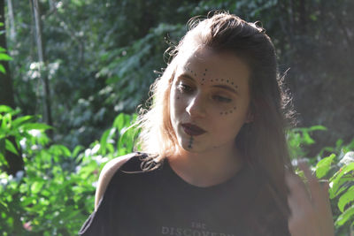 Portrait of young woman looking away against plants