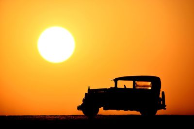 Silhouette truck on field against orange sky